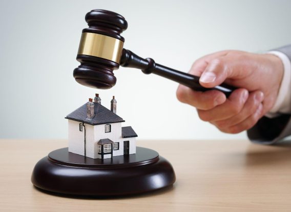 A gavel being used to auction a small model house, representing real estate bidding in a legal context