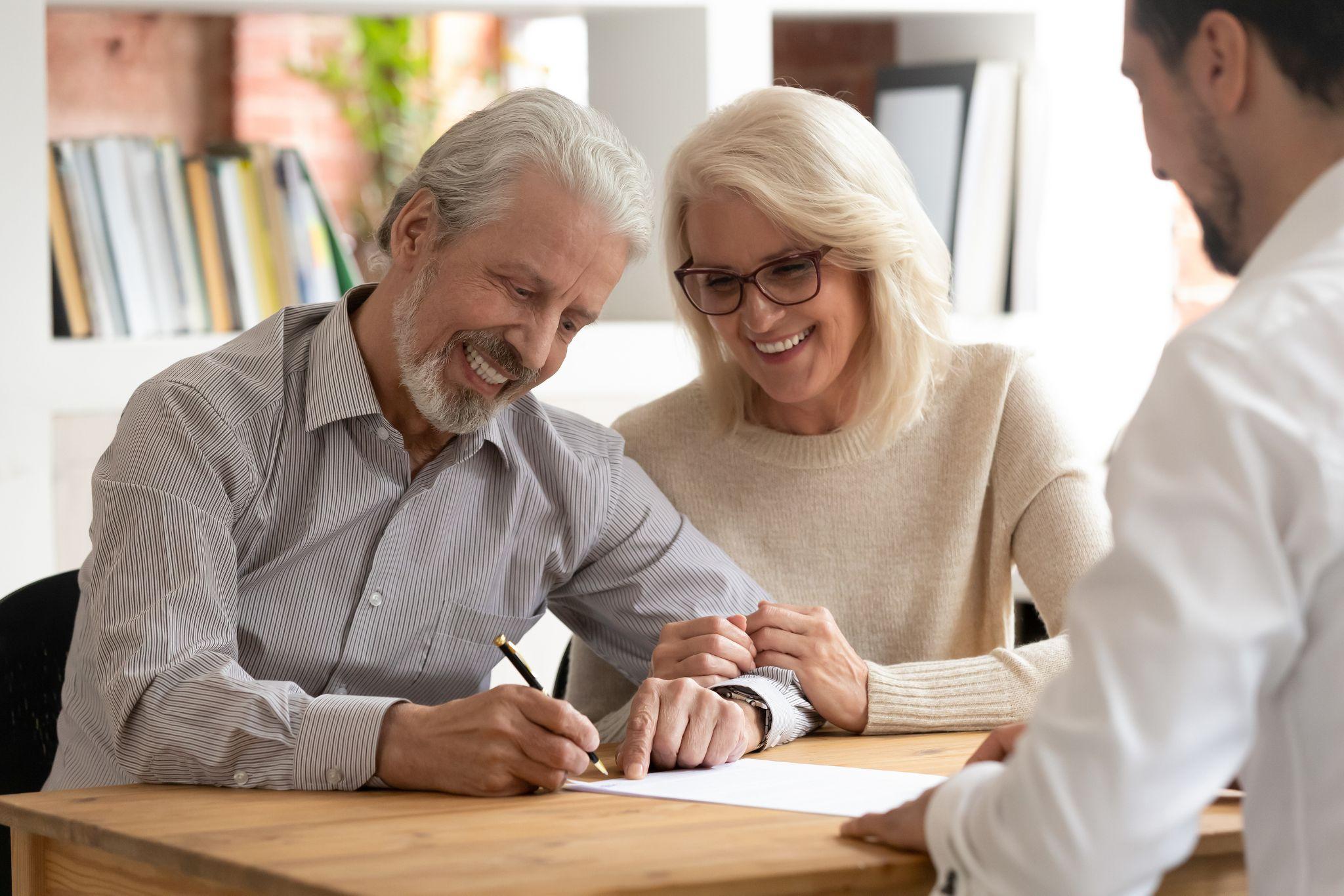 A happy older couple signing real estate documents, emphasizing the role of property trusts in securing and transferring assets