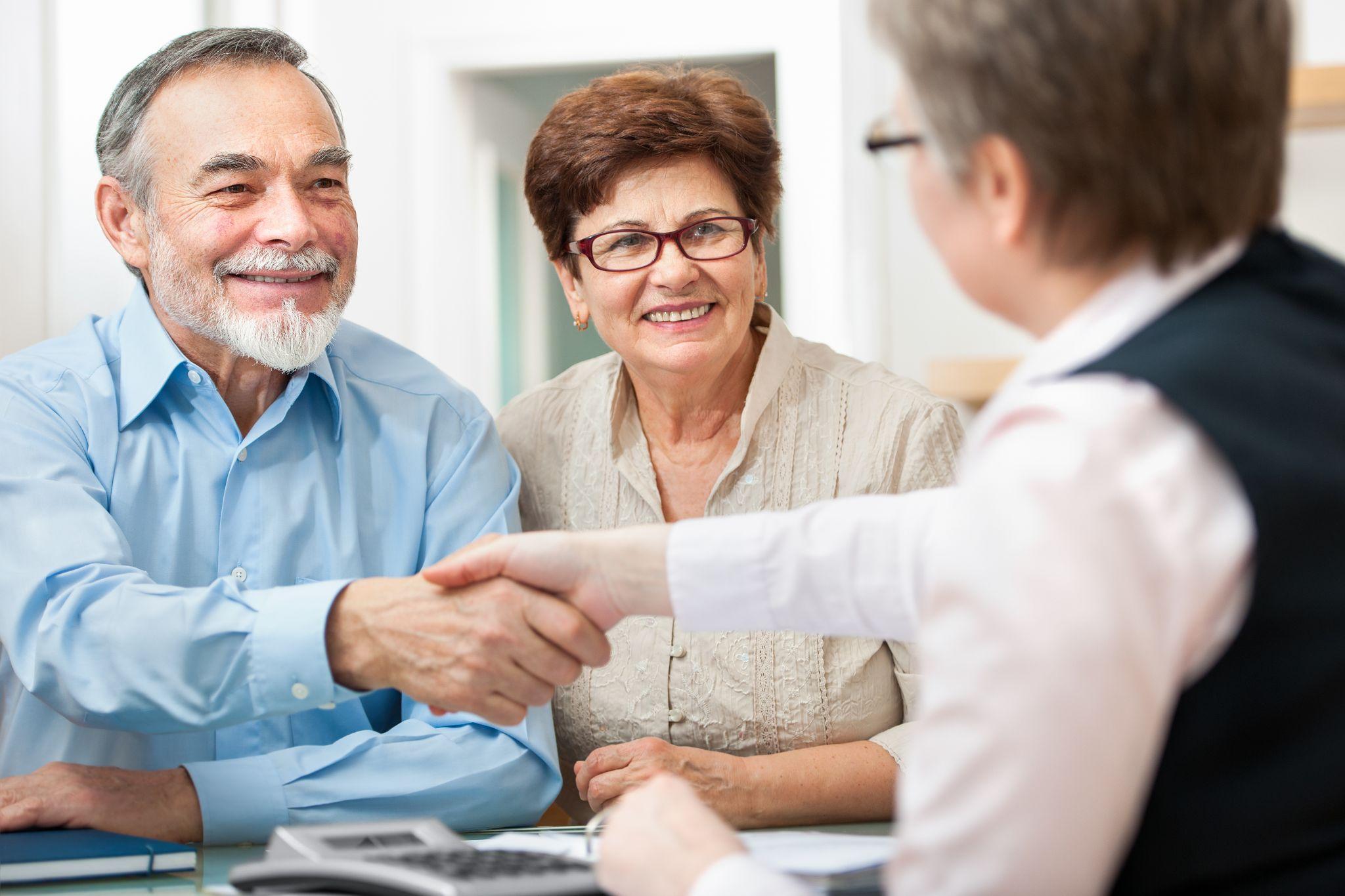 A senior couple shaking hands with a lawyer, likely finalizing real estate or estate planning matters